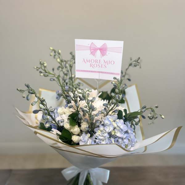 Bouquet of pale blue and white flowers wrapped in white paper with a ribbon