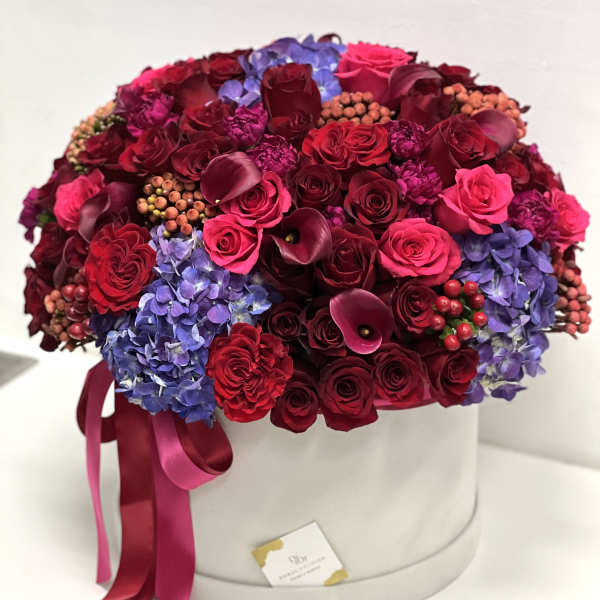 Round box arrangement of red roses, purple hydrangeas, and dark calla lilies