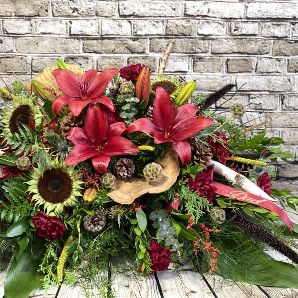 Large red floral arrangement with lilies and sunflowers, accented by ribbons