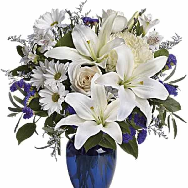 White lilies and daisies arranged in a blue glass vase