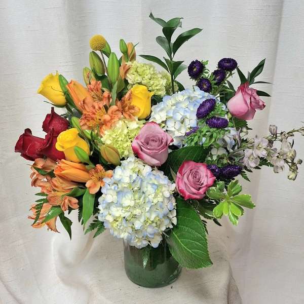 Mixed bouquet of roses, hydrangeas, lilies and other blooms in a clear glass vase