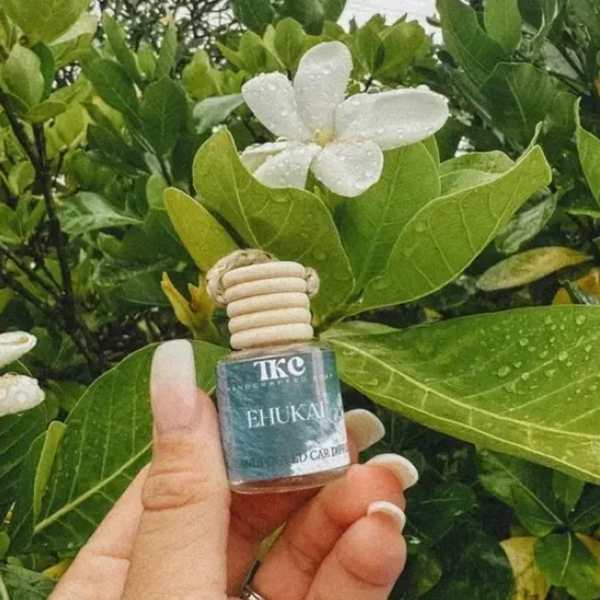 White flower among glossy green leaves with a small hanging bottle held in front