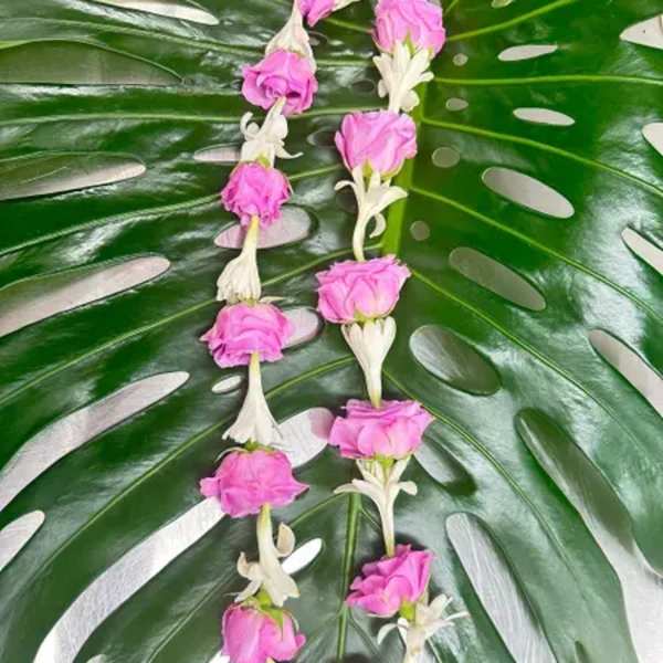 Pink flower garlands laid over large split monstera leaves