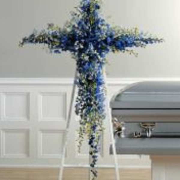Blue and white floral cross-shaped funeral spray on an easel
