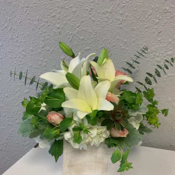 White lilies and pale pink roses arranged in a square vase