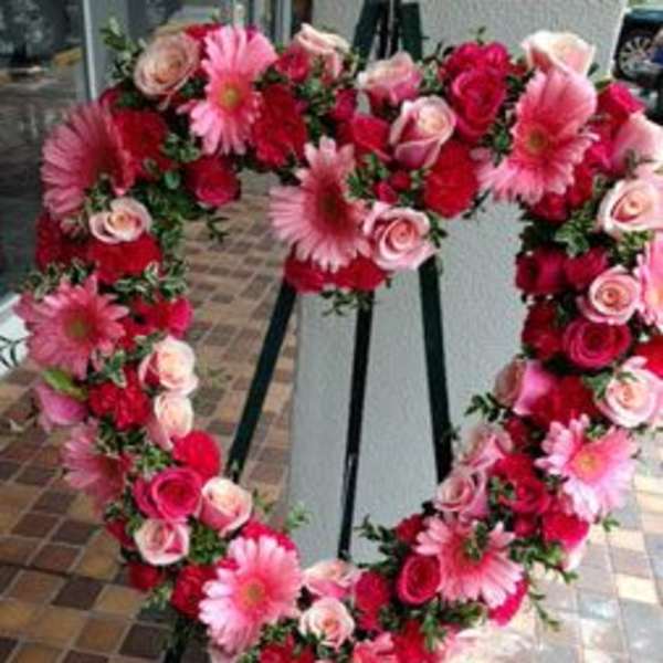 Heart-shaped floral wreath with pink and red roses and daisies on an easel