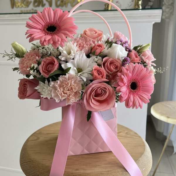 Pink and white flower arrangement in a pink gift bag with ribbon handles