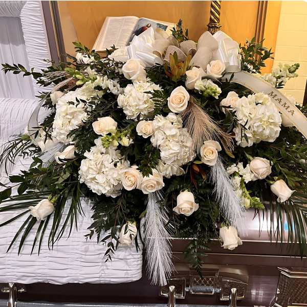 Large white rose and hydrangea casket spray with ribbon and plumes on a closed casket