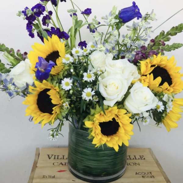 Bouquet of sunflowers, white roses, and purple flowers in a glass vase