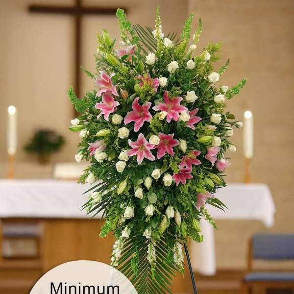 Tall standing spray with pink lilies and white roses on a metal easel in a church.