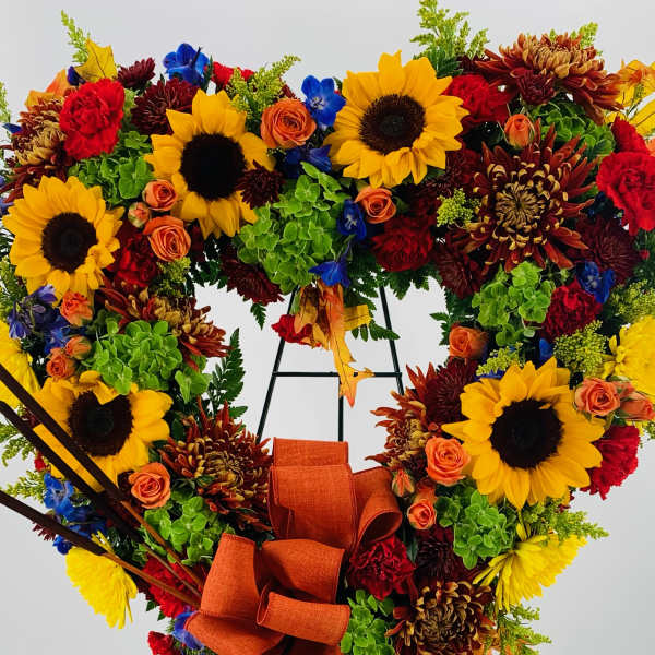 Heart-shaped floral wreath with sunflowers, roses, and an orange ribbon on an easel