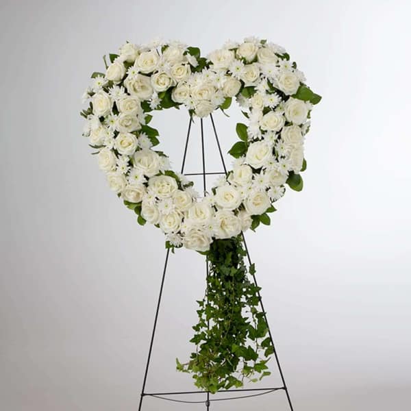 Heart-shaped white rose wreath on a stand with trailing greenery
