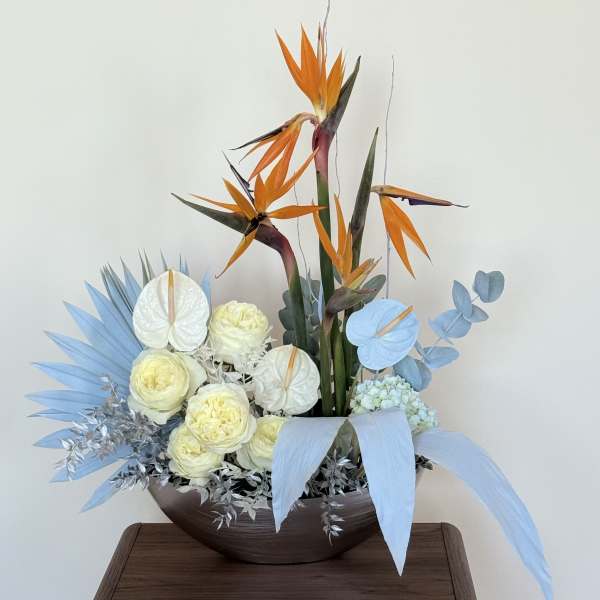 Tropical floral arrangement with orange bird-of-paradise and pale blooms in a bowl vase