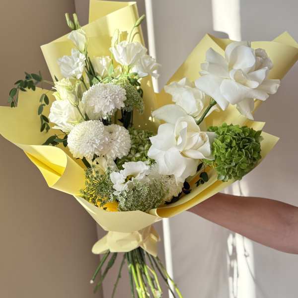 White bouquet with roses, chrysanthemums, and green hydrangea wrapped in yellow paper