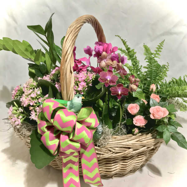 Basket of pink orchids, peach roses, and blooming plants with a large green and pink bow and small bird accent