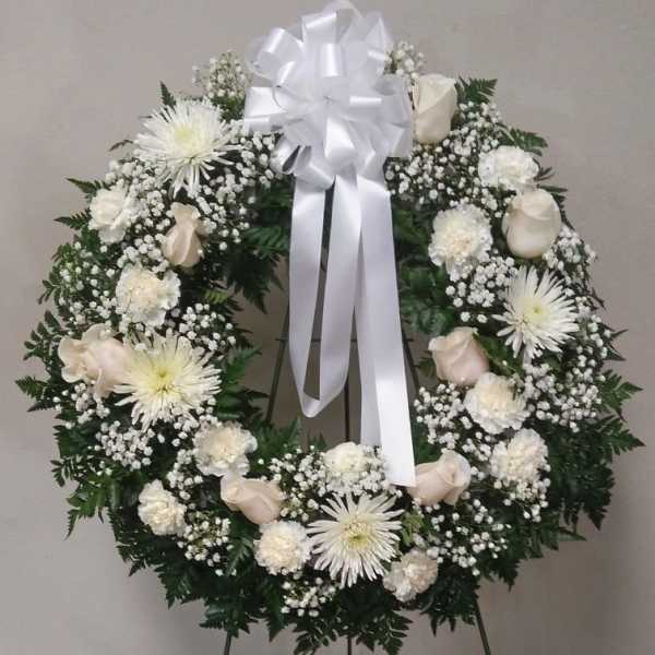 White funeral wreath with roses, daisies, and a large ribbon bow