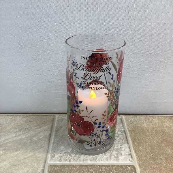 Lit memorial candle in a floral glass holder