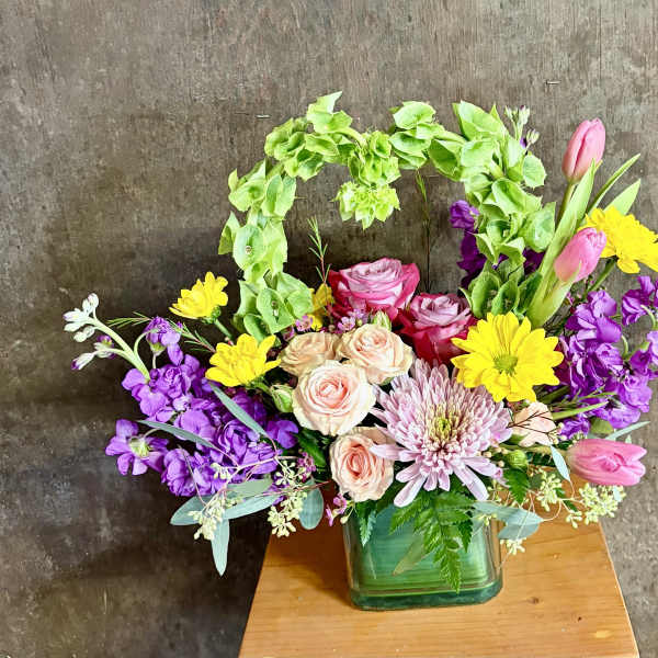 Mixed bouquet in a green glass vase with pink, yellow, and purple flowers