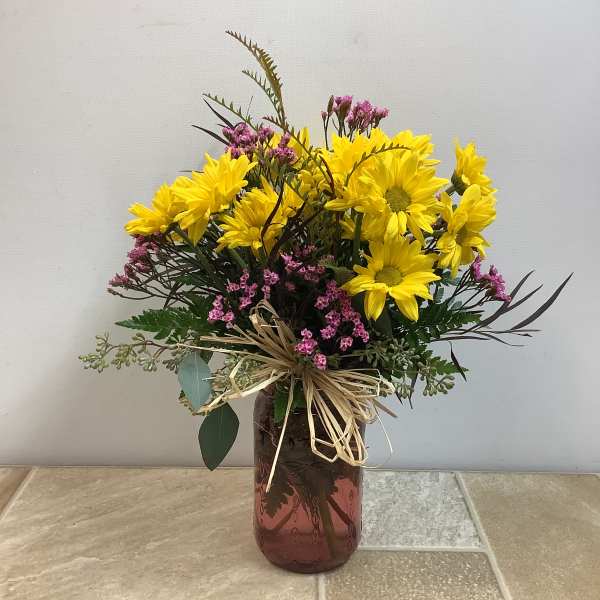Yellow daisy bouquet in a brown glass vase with pink filler flowers