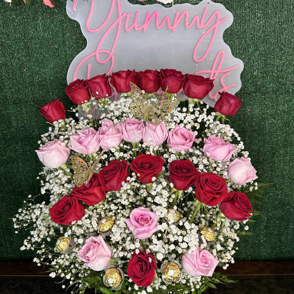 Pink and red roses arranged around a "Yummy" sign on a green backdrop