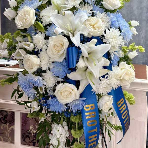 Standing floral spray of white lilies, roses, and blue flowers with a blue ribbon