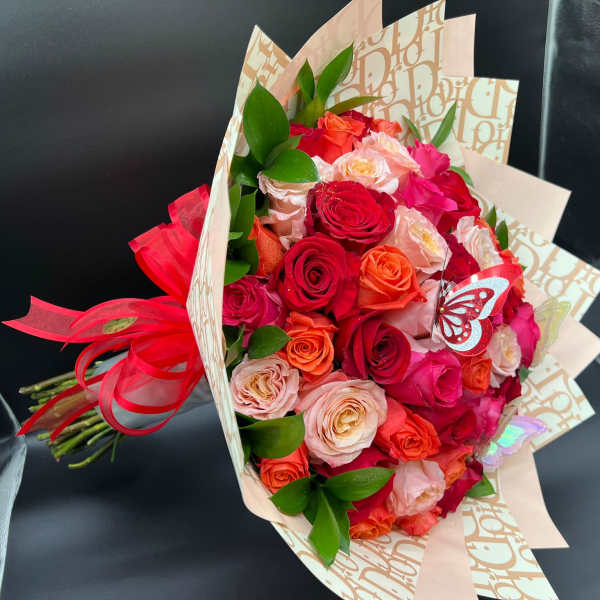 Bouquet of red, pink, and peach roses wrapped in patterned paper