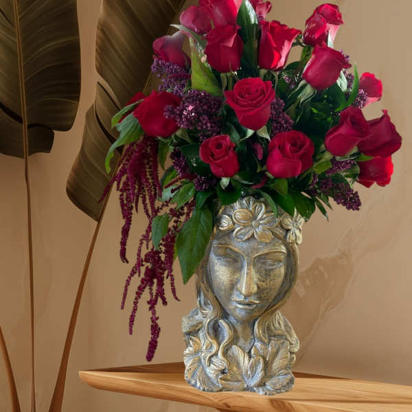 Red roses arranged in a decorative silver vase with purple filler flowers.