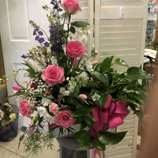 Tall bouquet of pink roses, purple flowers, and white blooms with a pink ribbon