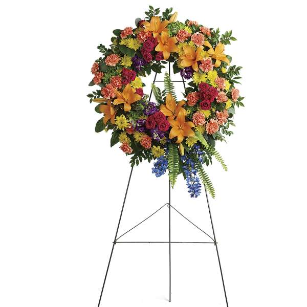 Standing floral wreath on an easel with orange lilies, roses, and mixed blooms