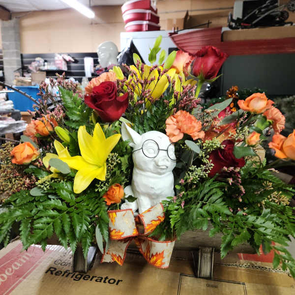 Mixed bouquet with yellow lilies, red roses, and orange carnations around a small white dog figurine
