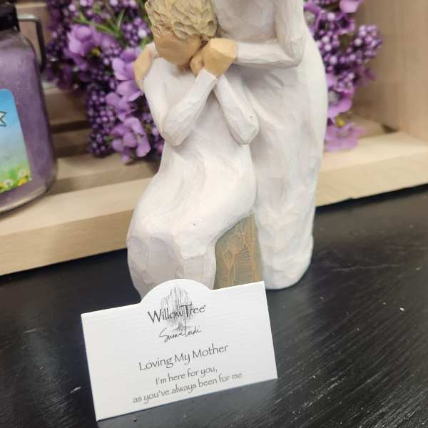 Wooden figurine of a mother and child with a purple floral wreath behind it