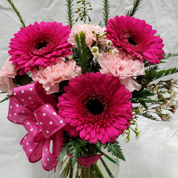 Pink gerbera and carnations in a glass vase with a polka-dot ribbon