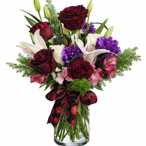 Bouquet of red roses, white lilies, and purple flowers in a glass vase
