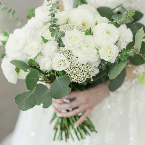 Bride holding a white bouquet with roses and greenery