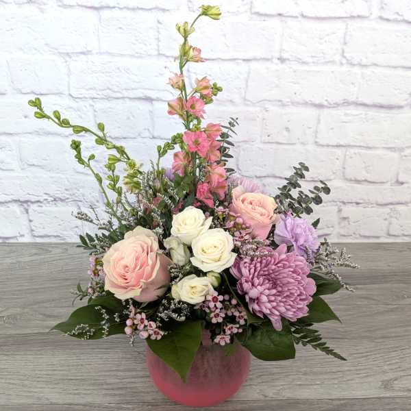 Pink and white roses with purple blooms in a pink vase