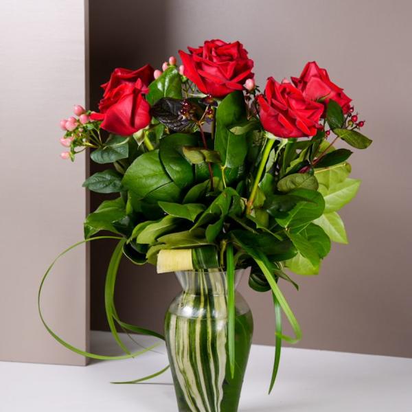 Red roses arranged in a clear glass vase with green foliage