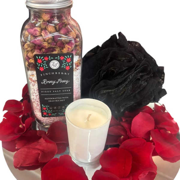 Rose petals with a bath soak jar, candle, and black bath pouf on a tray