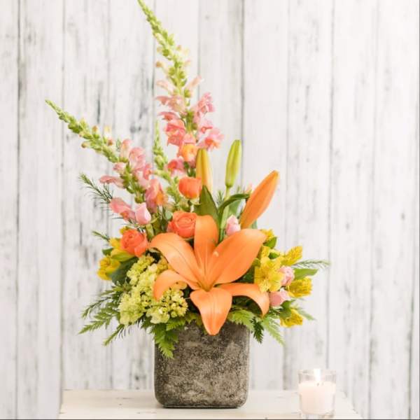 Orange lilies and pink flowers arranged in a gray vase
