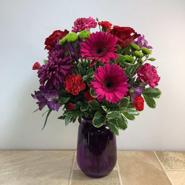 Mixed bouquet of pink, red, and purple flowers in a purple glass vase