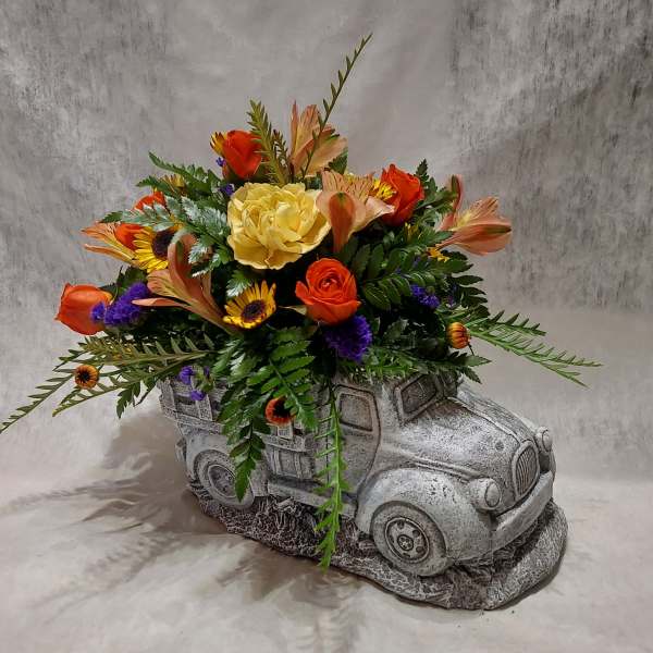 Orange and yellow flowers arranged in a gray truck-shaped planter