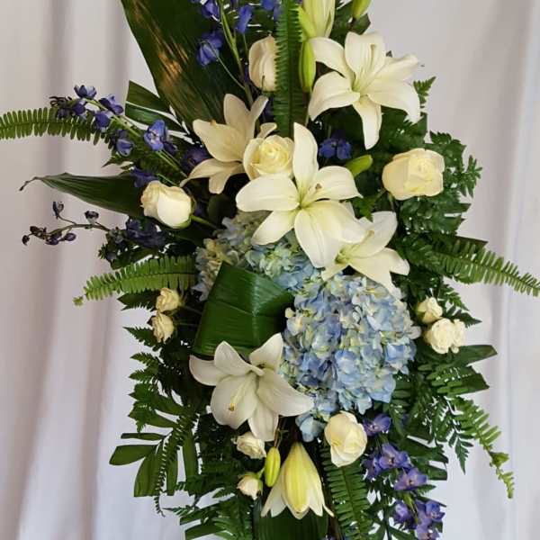 Tall floral standing spray with white lilies, roses, blue hydrangea, and purple delphinium