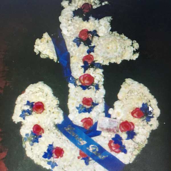 Floral arrangement shaped like a cross with white flowers, red roses, and blue ribbon
