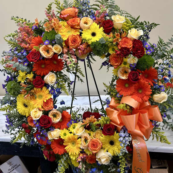 Large floral wreath with roses, gerbera daisies, and mixed blooms on a stand
