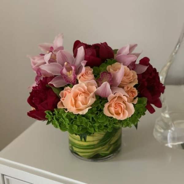 Compact bouquet of pink orchids, peach roses, and deep red blooms in a glass vase