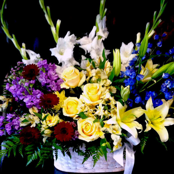Tall mixed basket arrangement with yellow roses, lilies, white gladiolus, and blue delphinium.