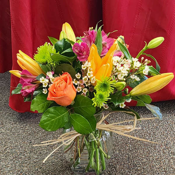Mixed bouquet of lilies, roses, and small white flowers in a glass vase