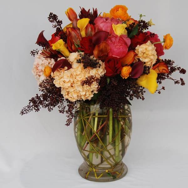 Mixed bouquet of red, pink, and yellow flowers in a clear glass vase