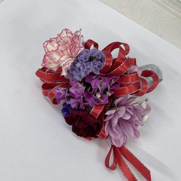 Small corsage with pink, purple, and burgundy flowers tied with red ribbon