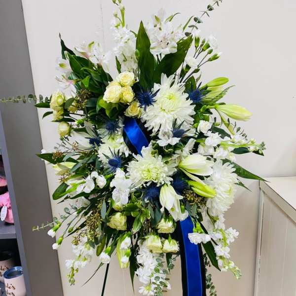 Large white floral standing spray with blue ribbon on an easel