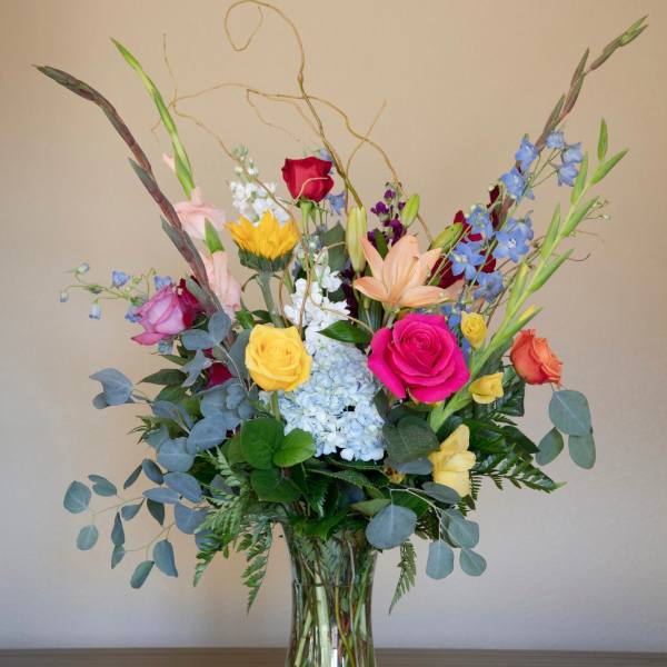 Mixed bouquet of roses, lilies, hydrangea, and blue delphinium in a glass vase